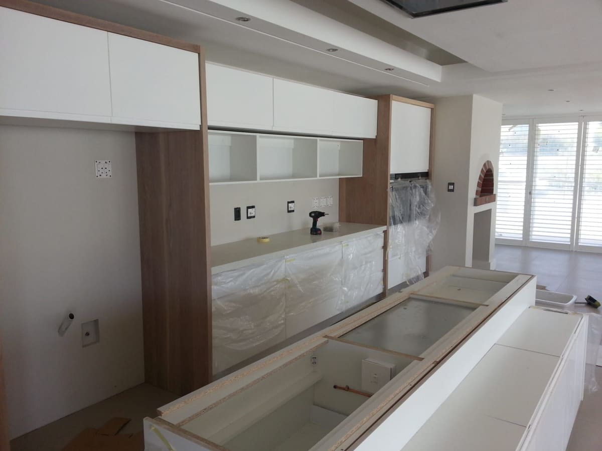 Installation in progress: a long island in protective wrapping in front of wall units and open shelving being fitted.