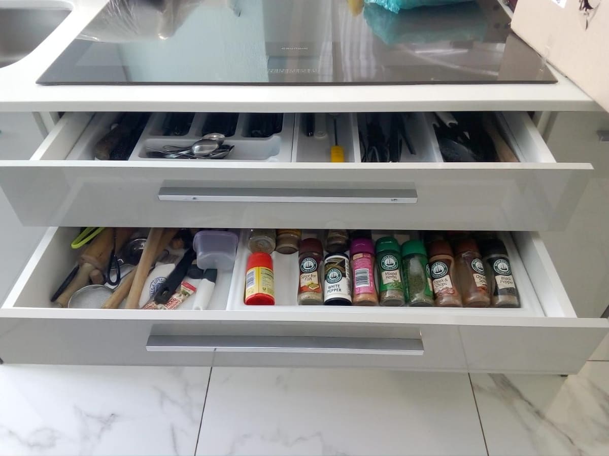 Two open white gloss drawers with a cutlery insert and a spice organiser, under an induction hob.