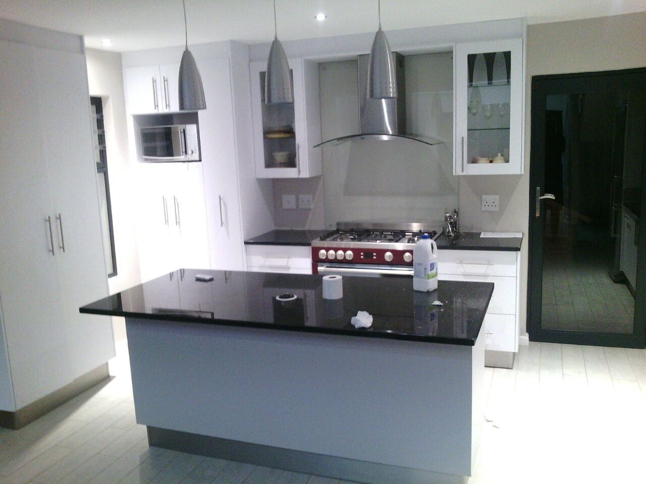 White kitchen with an island topped in black stone, a range cooker, a curved glass extractor and three metal pendant lights.