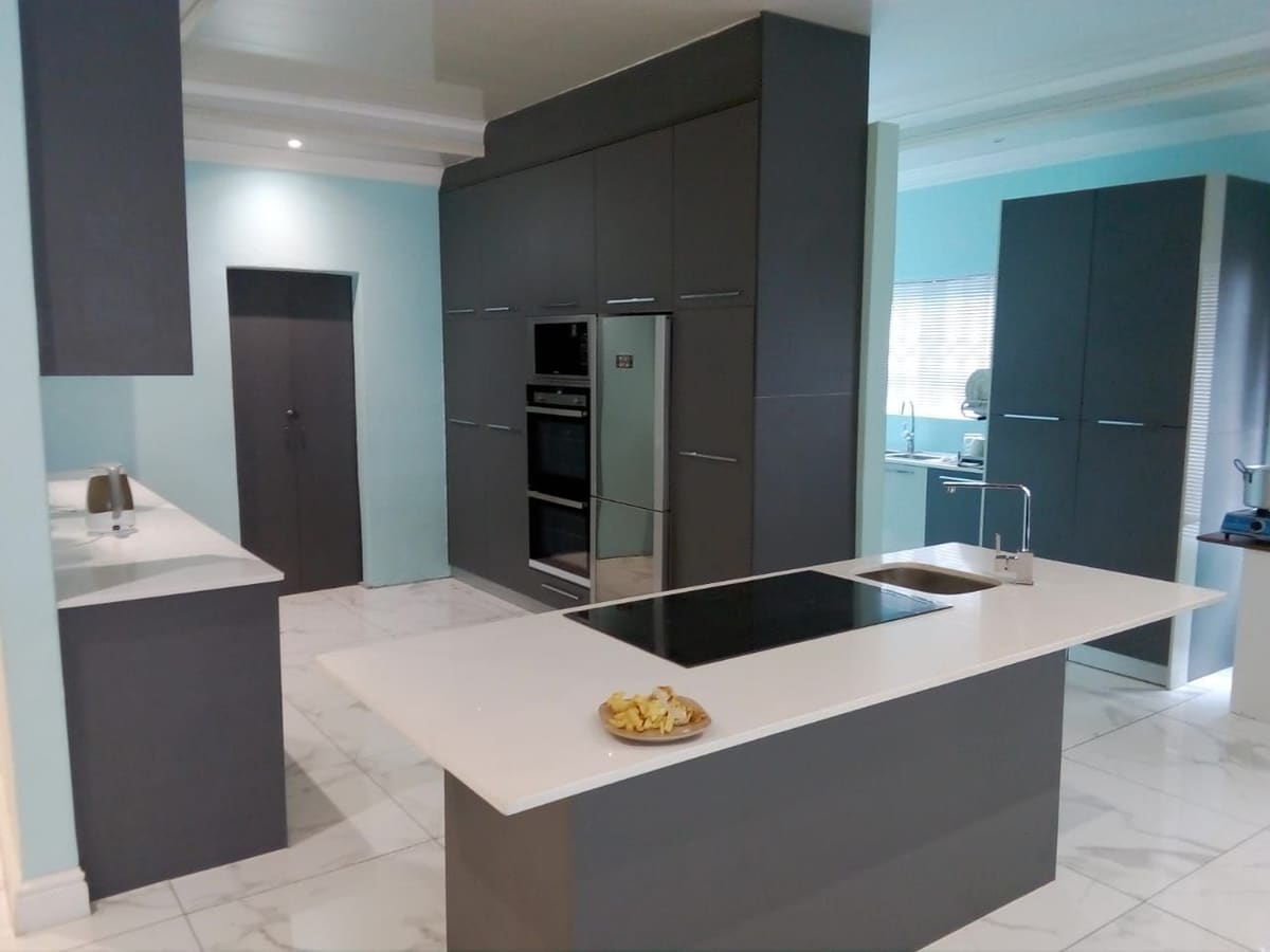 Kitchen with charcoal tall units housing a double oven and fridge, and a white island with an induction hob and sink set into a charcoal base.