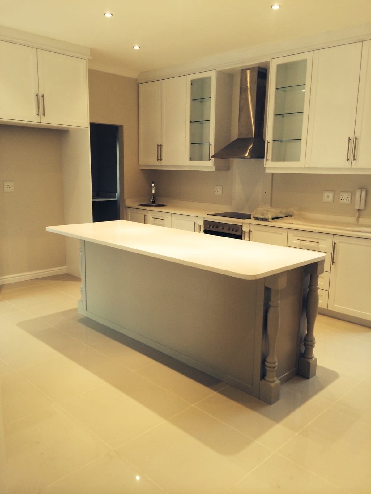 Cream kitchen with glass-fronted wall units, a chimney extractor and a long island on turned legs with a pale stone top.