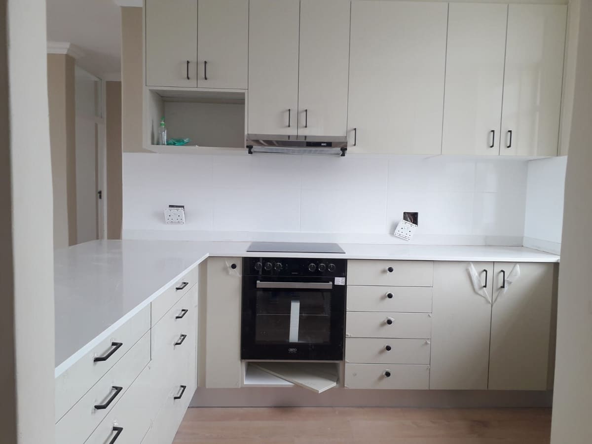 Cream kitchen with wall units, a built-in oven, drawers and a white worktop along an L-shaped run.