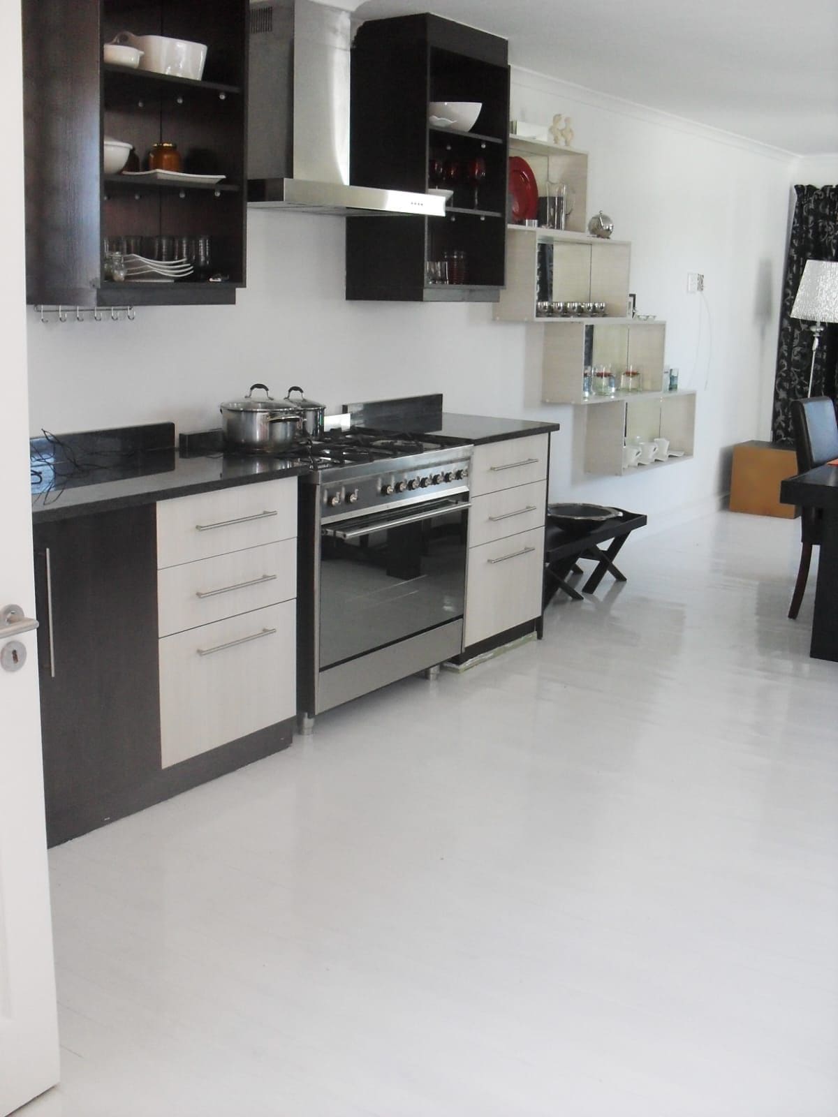 Kitchen with dark open shelving units either side of a steel extractor, a range cooker and pale drawer fronts.