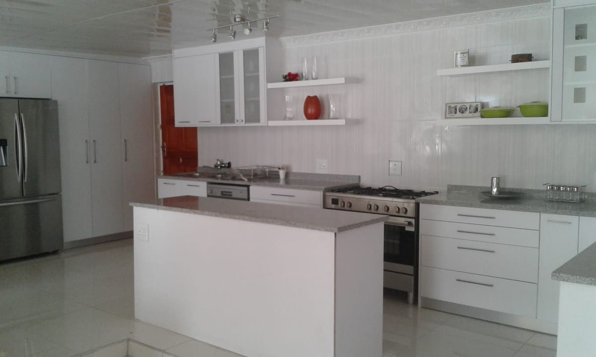 White kitchen with an island, grey worktops, open shelving on a white panelled wall and a range cooker.