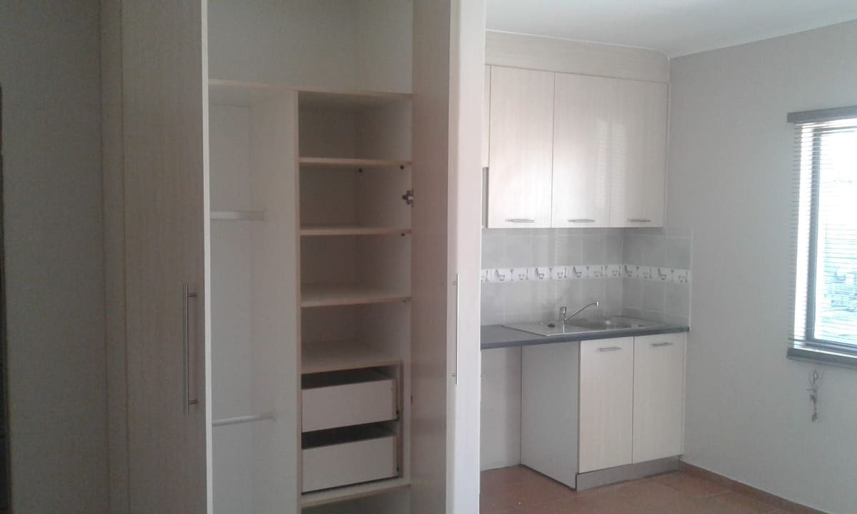 A tall built-in unit opened to show adjustable shelving and drawers, beside a kitchen run with wall units.
