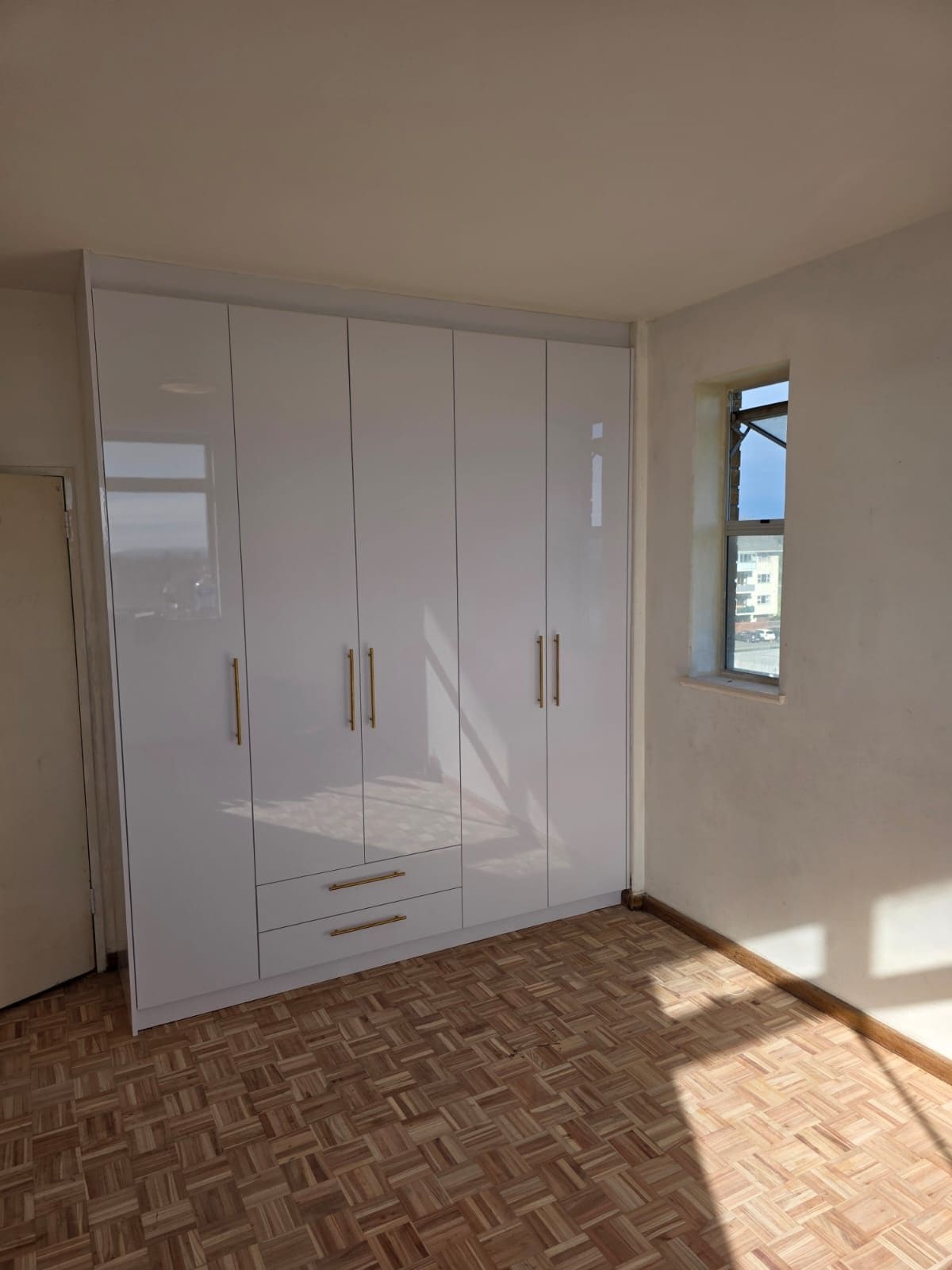 Floor-to-ceiling built-in wardrobe with white high-gloss doors, long brushed handles and two drawers, fitted wall to wall in a bedroom.
